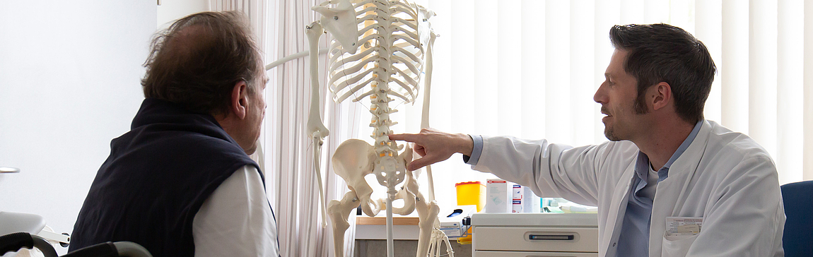 Dr. Buchmann erklärt einem Patienten die Wirbelsäule