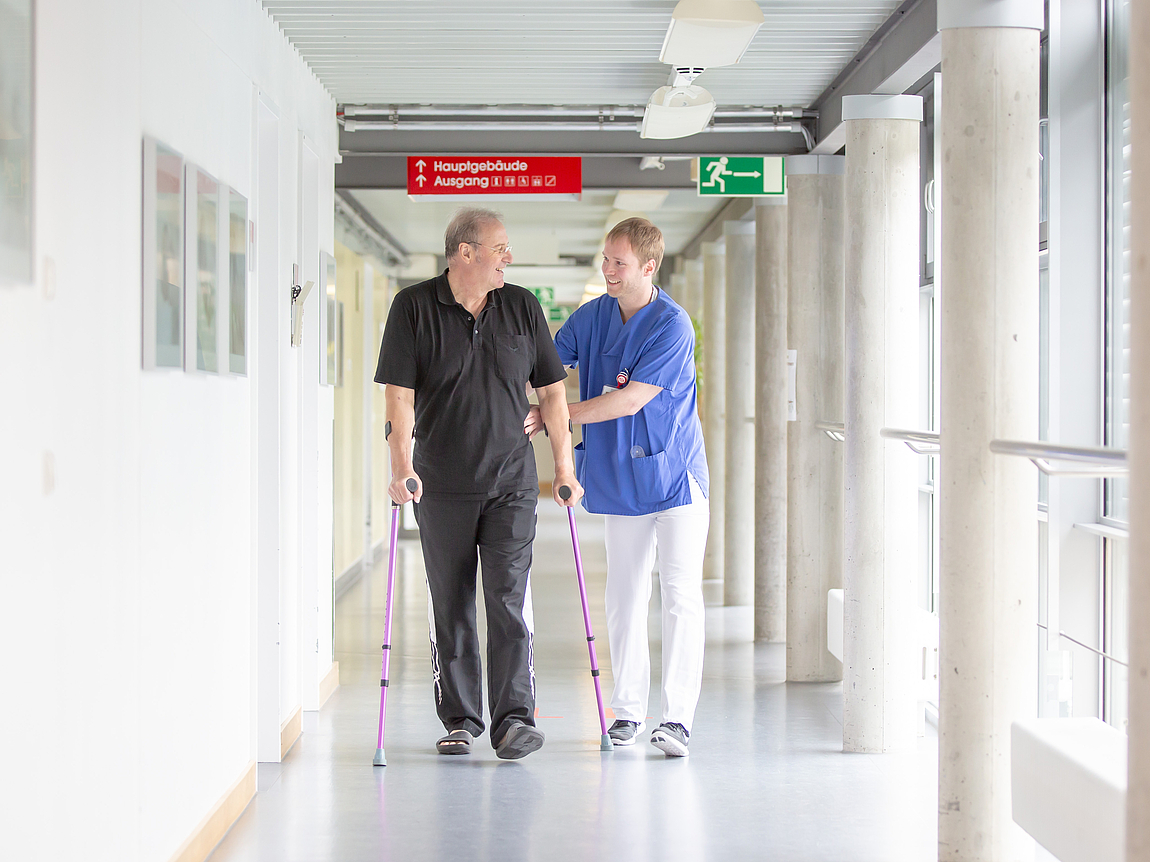 Patient mit Krücken erhält Unterstützung beim Gehen durch Therapeuten