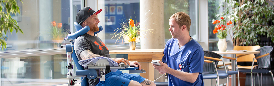 Fachkraft im Gespräch mit einem Patienten im Rollstuhl