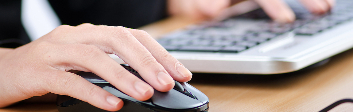 Hände einer jungen Frau an Tastatur und Computermaus