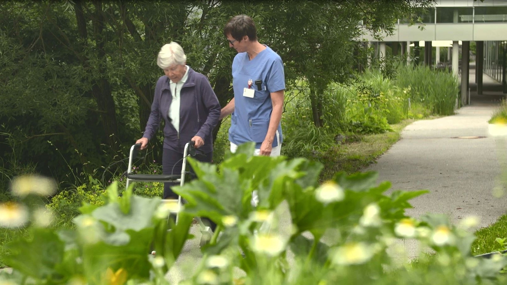 Ein Physiotherapeut macht einen Spaziergang mit einer älteren Patientin.